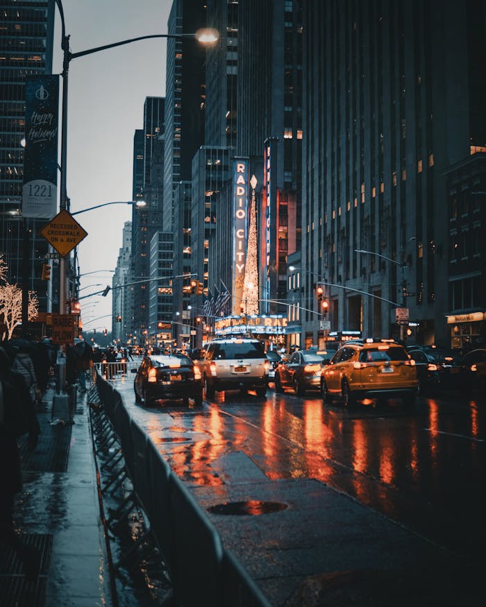 Dramatic city street view of New Yorks Radio City at night with reflections and taxis.