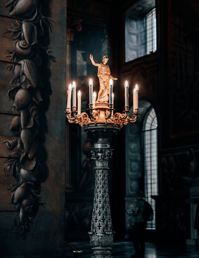 Home A detailed view of a golden statue candlestick in a dimly lit historic church interior.